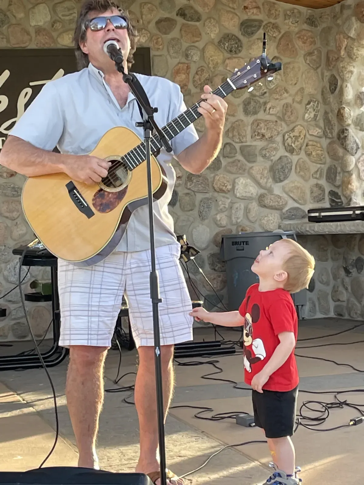 Paul Weidenbach performing outdoors with guitar alongside a young fan
