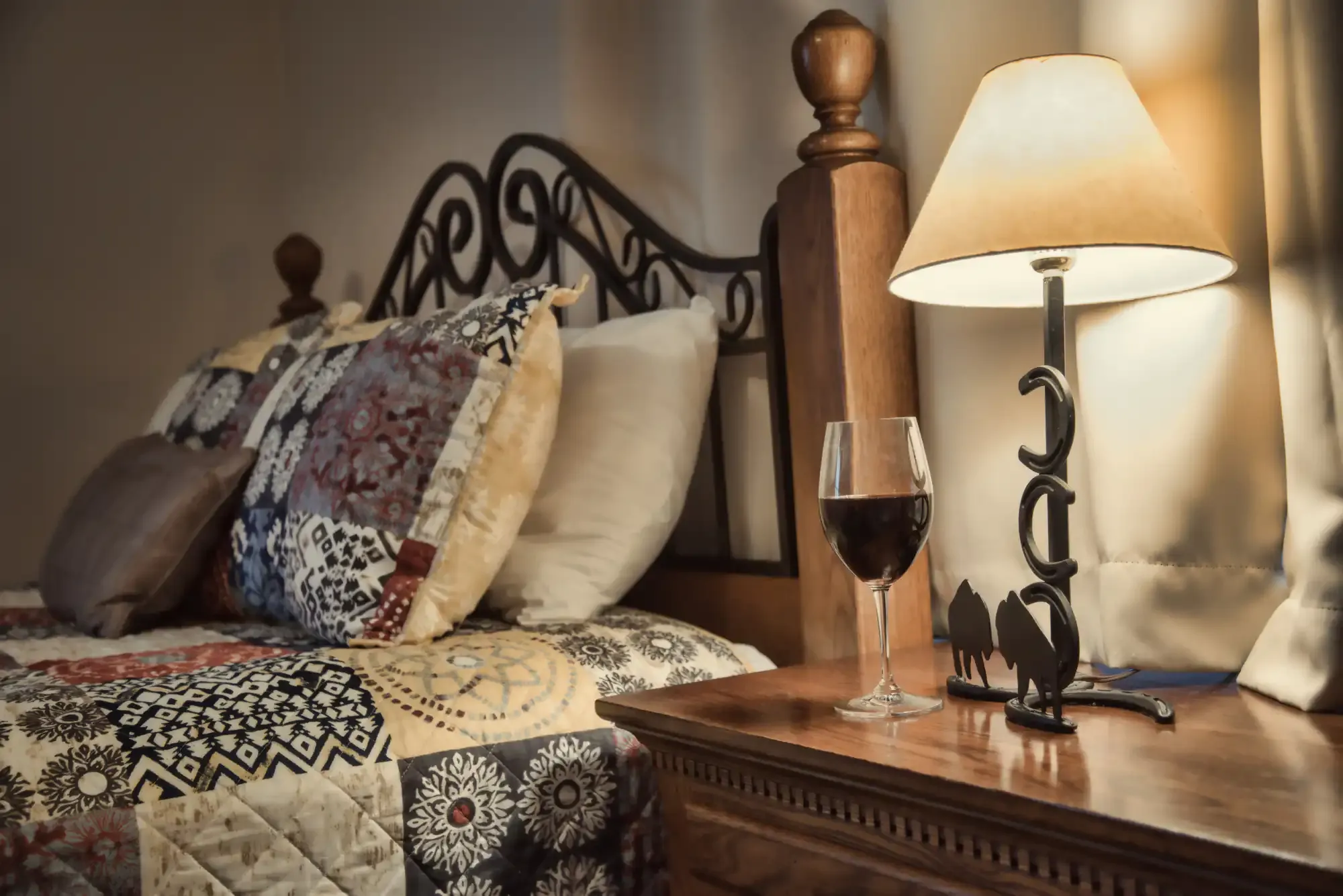 Wine glass next to a cozy bed with lamp